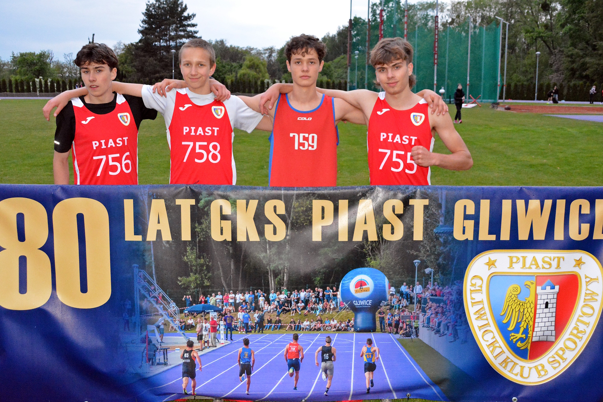 Fot. materiały piast.gliwice.pl czterej chłopcy w sportowych, czerwonych koszulkach przy banerze 80-lecia klubu