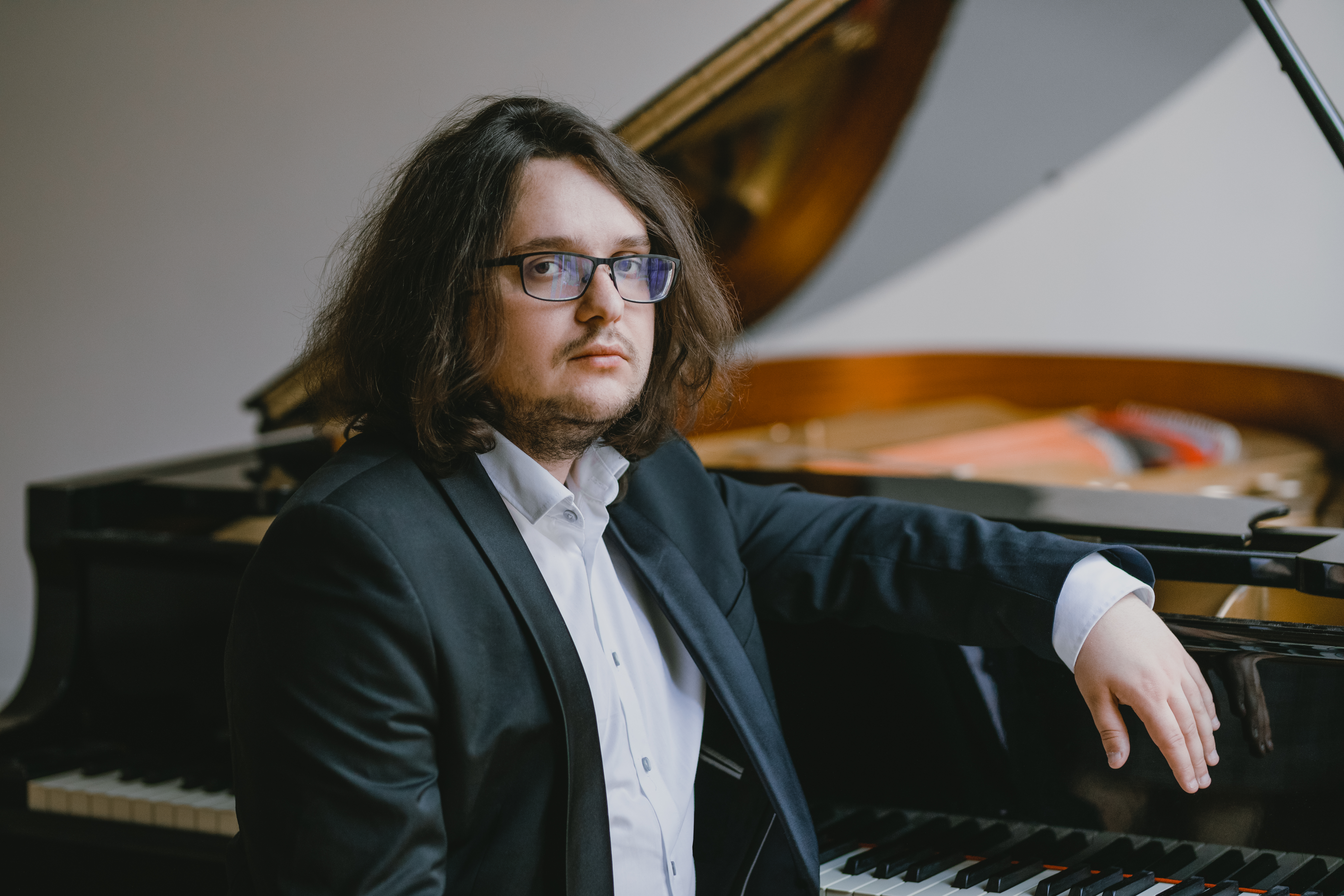Jakub Kuszlik siedzi oparty o fortepian