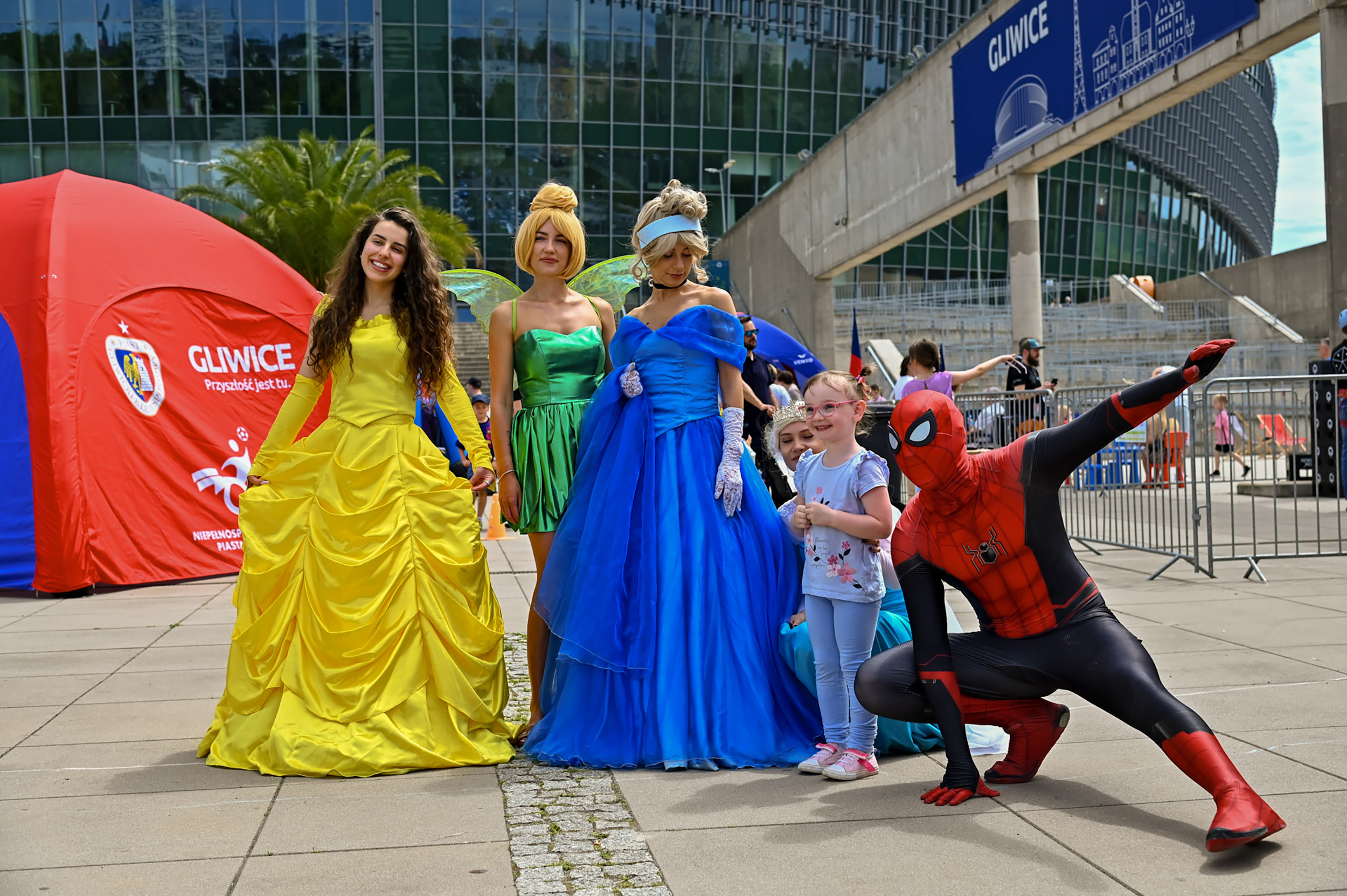 Postaci przebrane za księżniczkę Bellę, Kopciuszka, Dzwoneczka i Spidermana z dzieckiem pozują pod PreZero Areną Gliwice