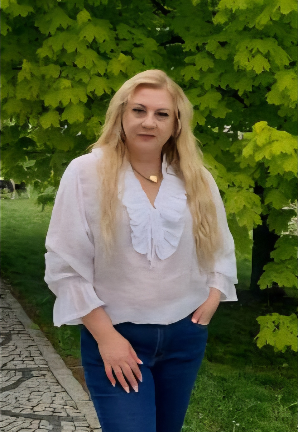 Kobieta o długich blond włosach ubrana w białą bluzkę i granatowe dżinsy