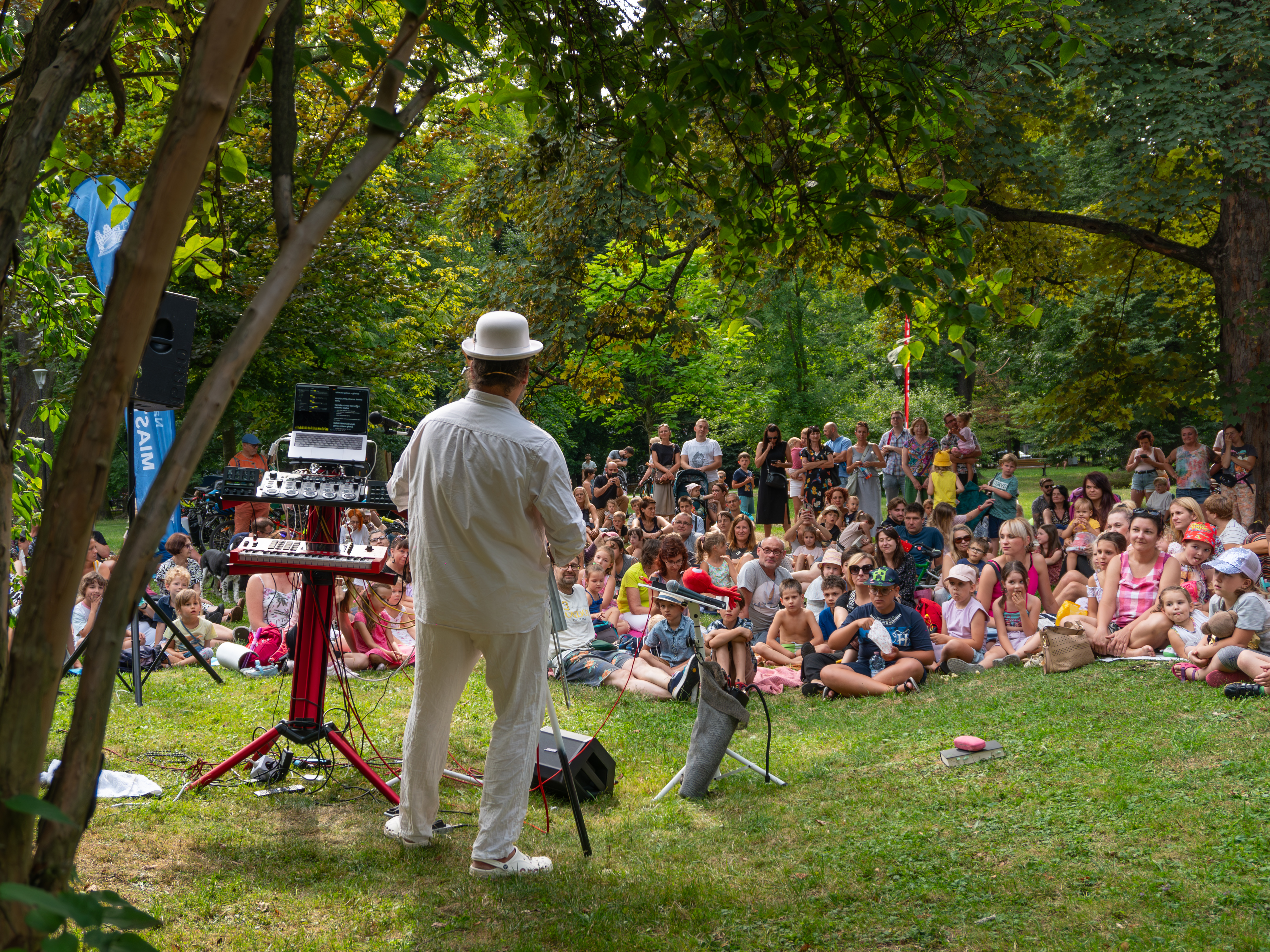 Artysta tyłem, stoi przed publicznością w parku