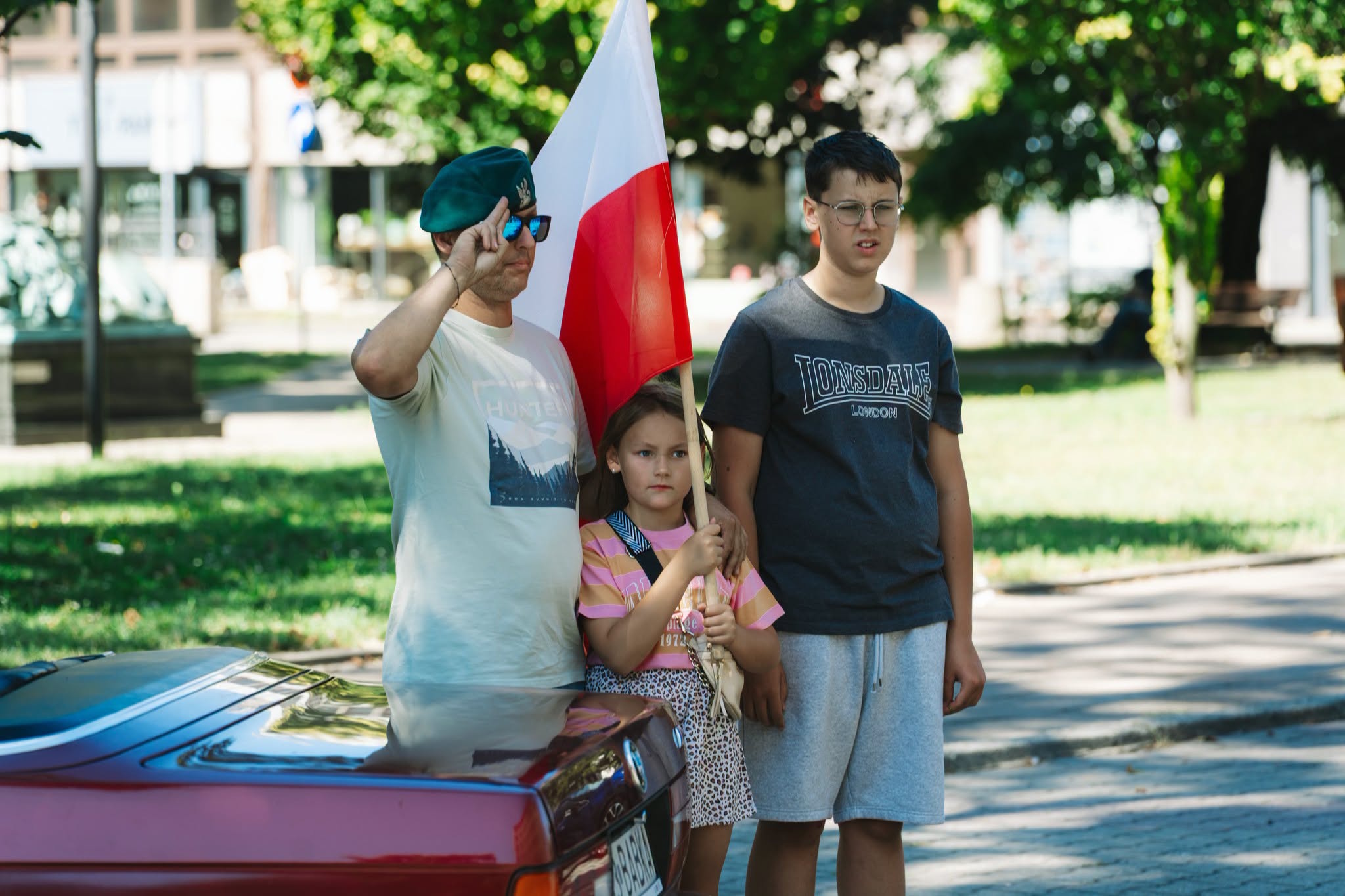 Ojciec z synami trzymający polską flagę i salutujący