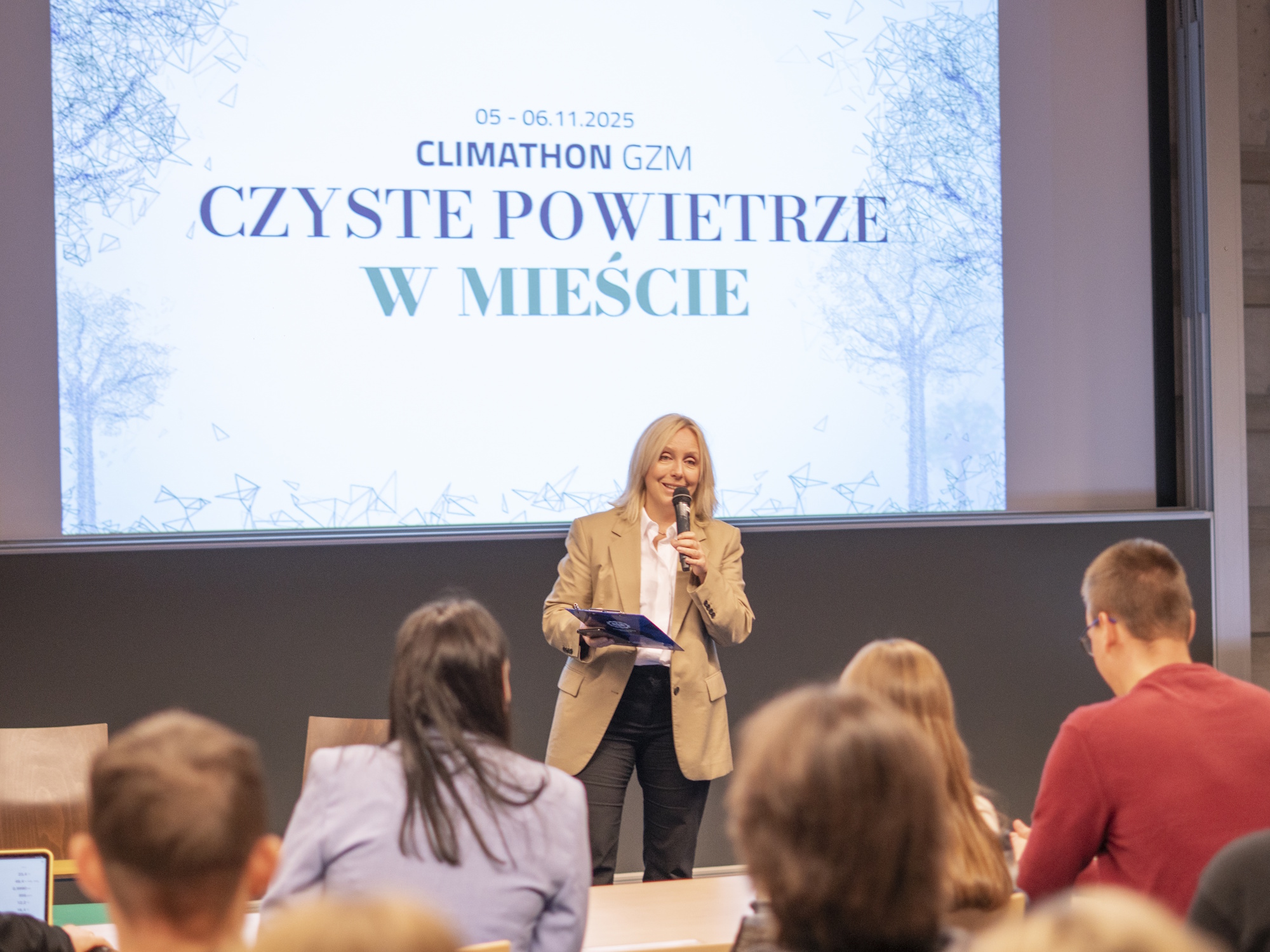 kobieta z mikrofonem przemawia, młodzi ludzie słuchają