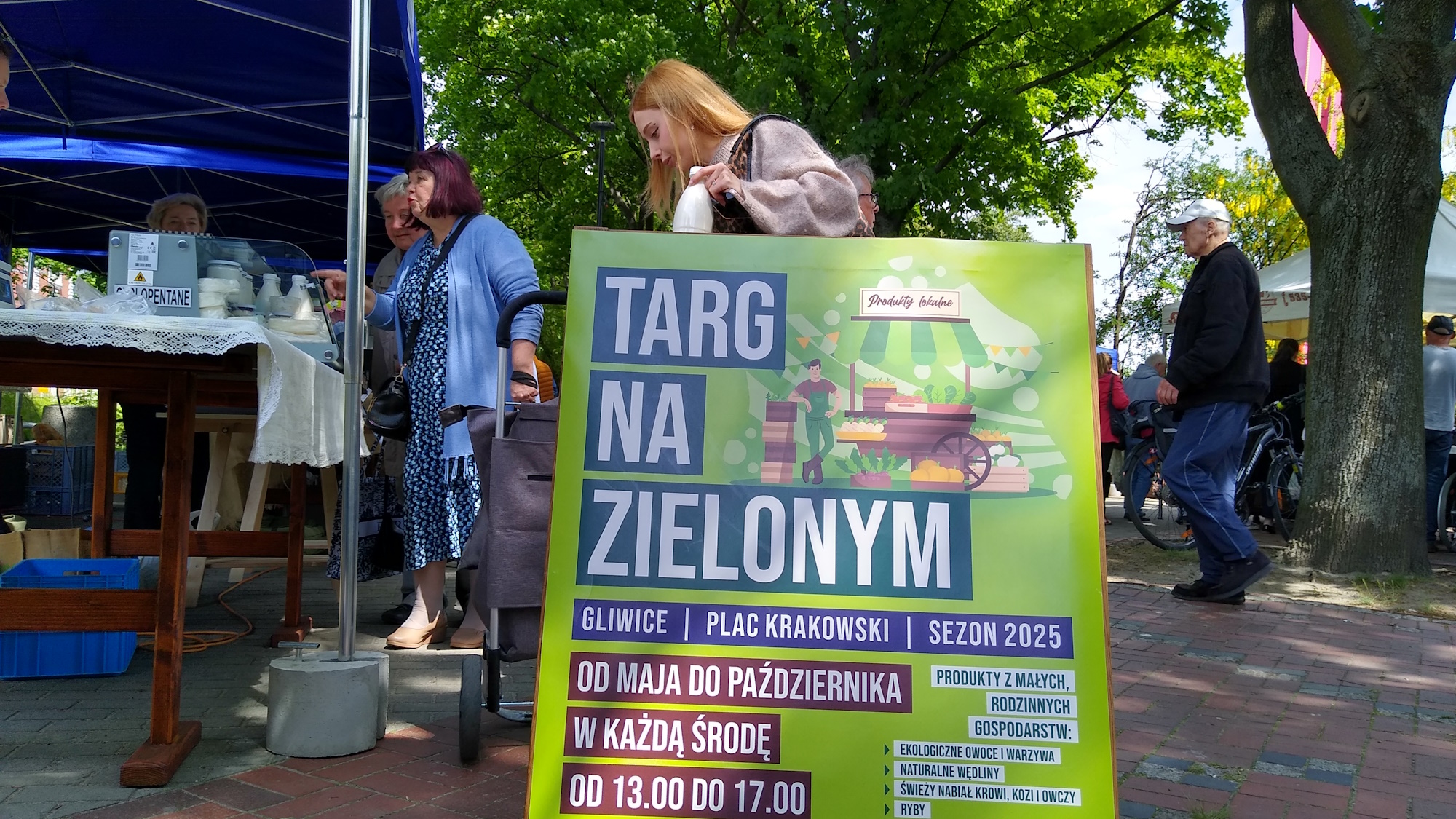 Fot. M.Foltyn/UM Gliwice tablica z informacją o godzinach działania targu i ludzie