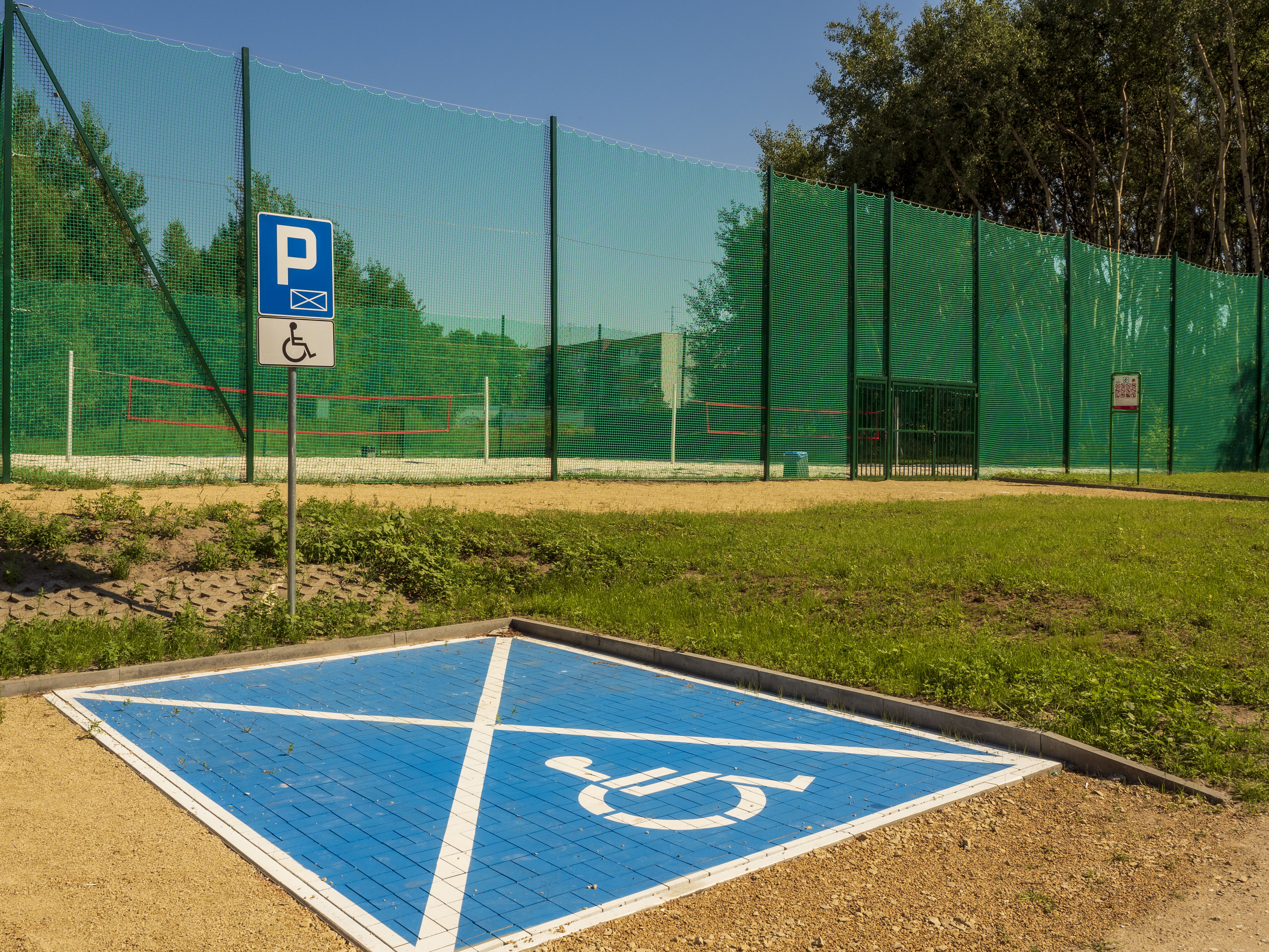 Miejsce parkingowe dla niepełnosprawnych z nowymi boiskami w tle