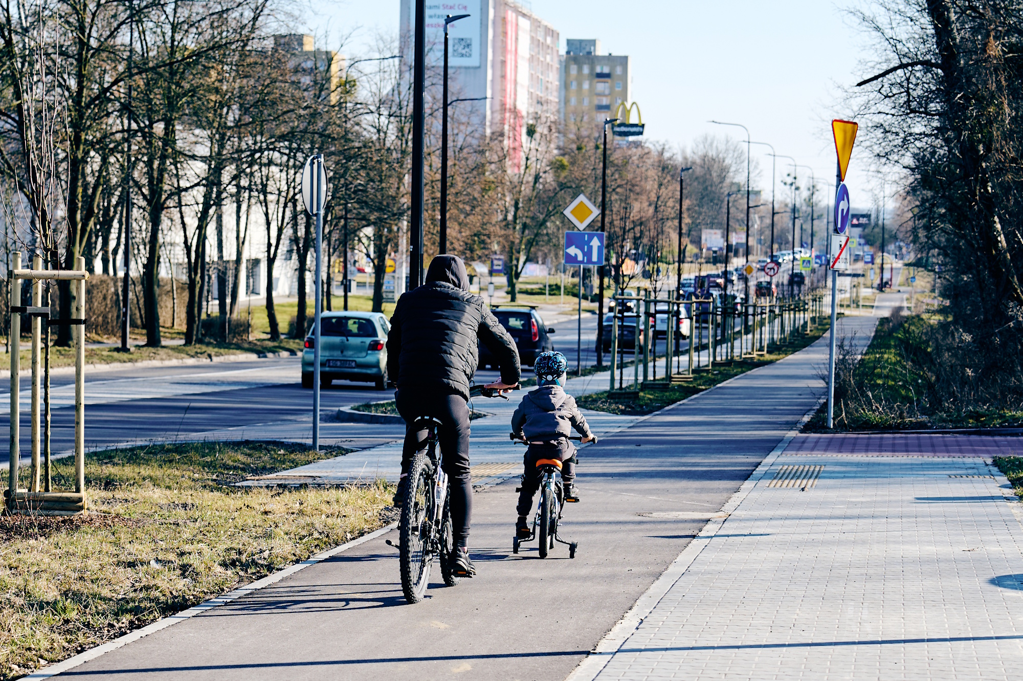dorosły rowerzysta z dzieckiem na rowerku czterokołowym na ścieżce rowerowej