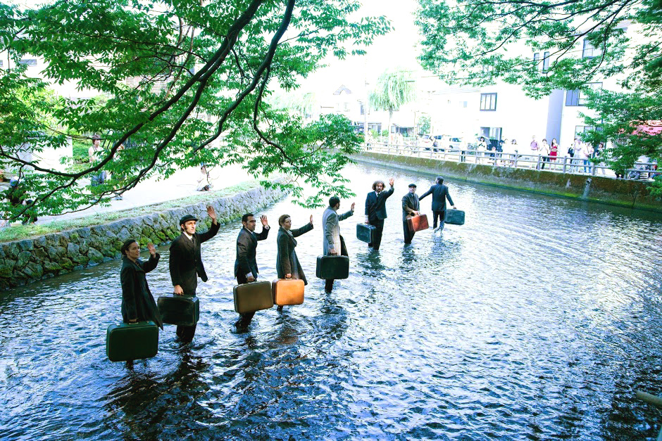 aktorzy z walizkami brodzą w wodzie