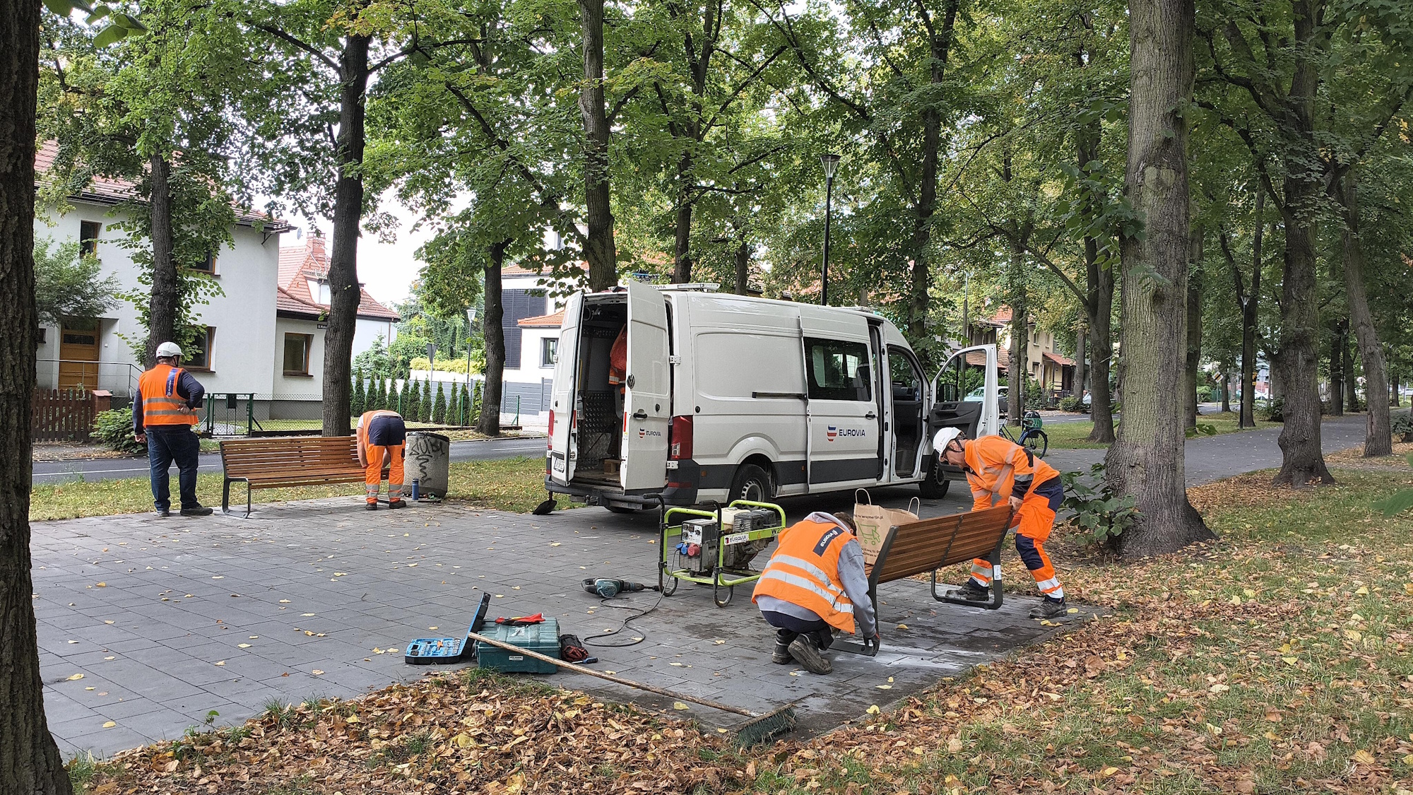 czterech robotników ustawia ławki w parku