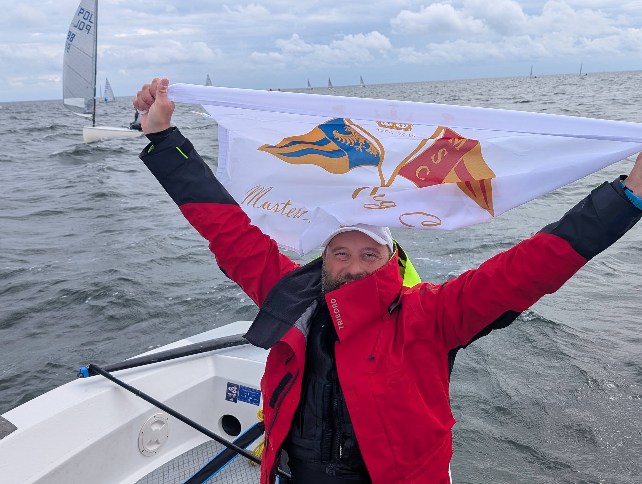 Bartosz Szydłowski na łodzi, rozpościerający flagę Masters of Sailing Clubu