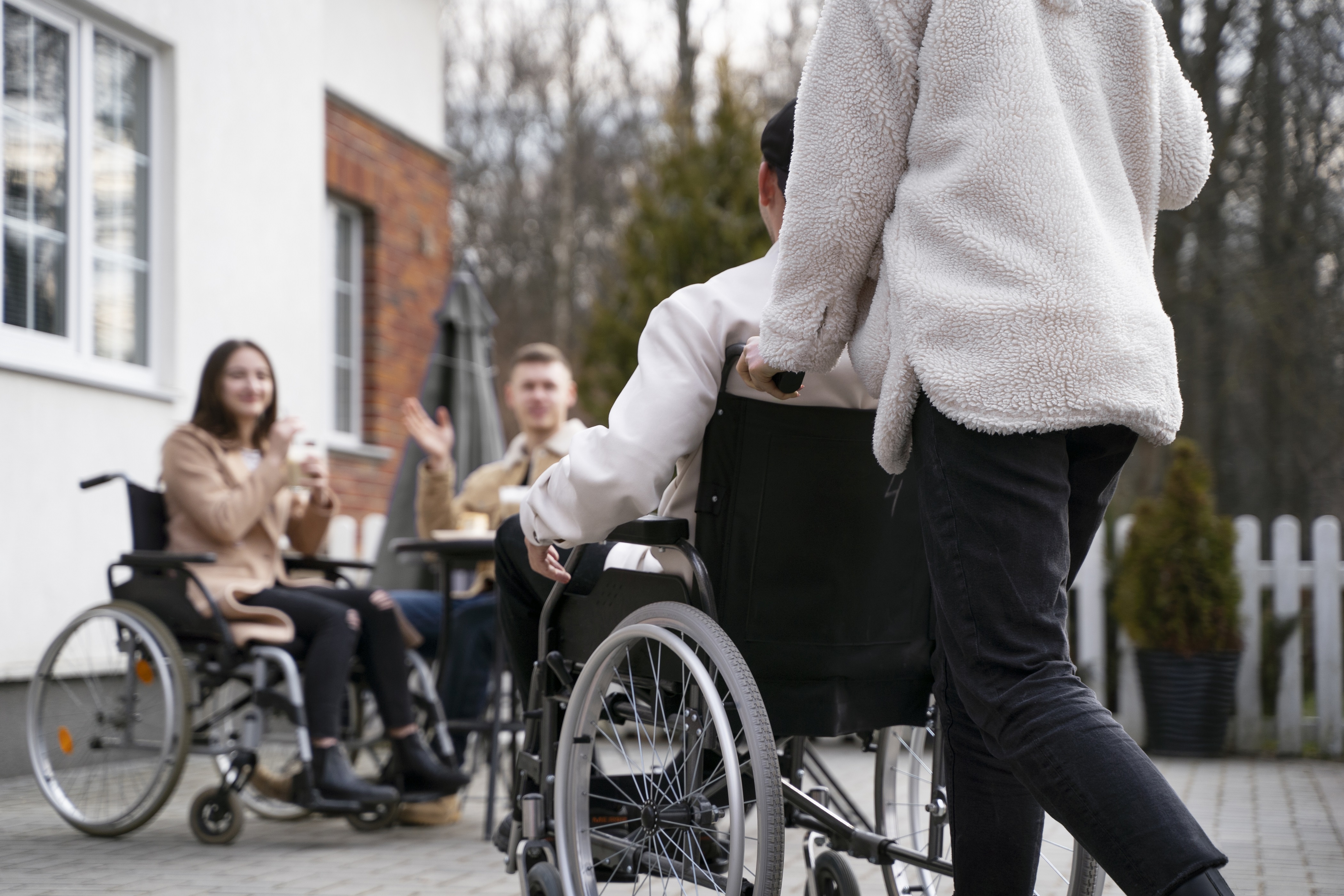 Osoba prowadząca podopiecznego na wózku do innych osób niepełnosprawnych