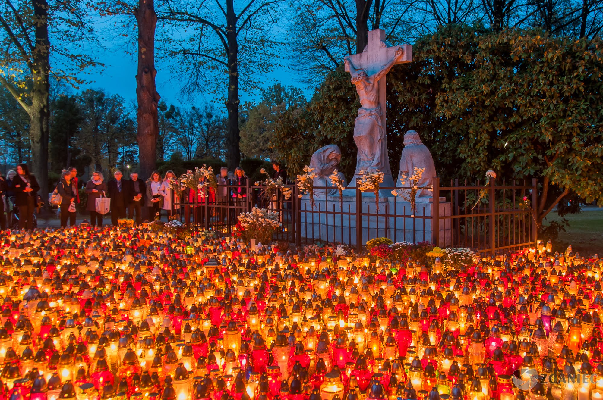 Mnóstwo zapalonych zniczy stojących pod cmentarnym zniczem
